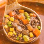 A soup ladle with ground beef soup inside of it in a pot of soup.