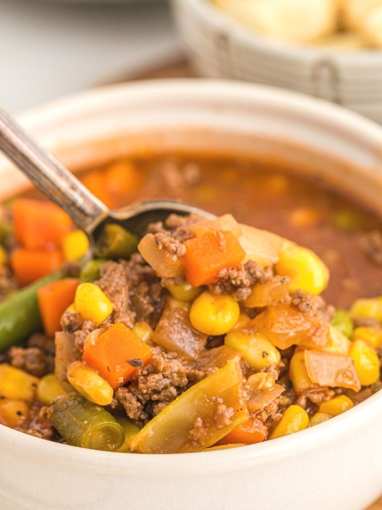 Close up shot of vegetable beef soup with a spoon holding some in it.