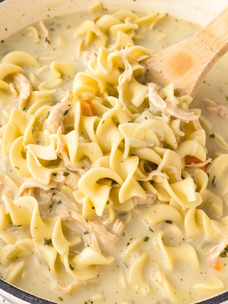 Creamy chicken soup with noodles inside a pot with a wooden spoon. 