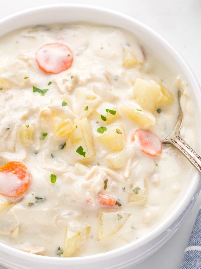 A bowl of soup with a spoon inside of it taking a scoop out. 