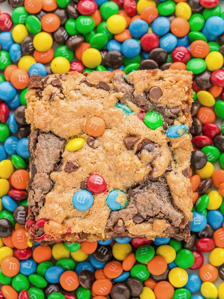 A brownie sitting atop a pile of m&m's candy in the background.
