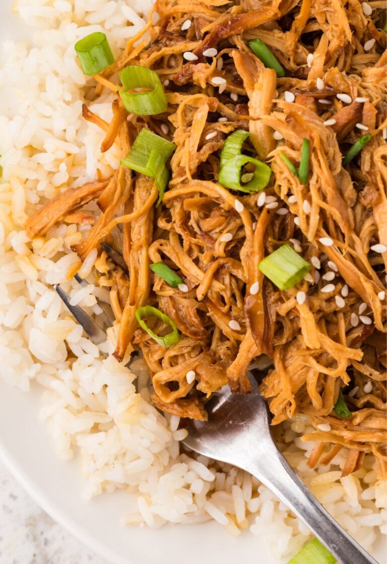A serving of white rice with sweet garlic chicken on top of it and a fork.