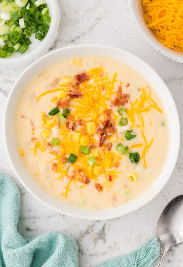 A bowl of chowder with cheese and green onions next to it in bowls.