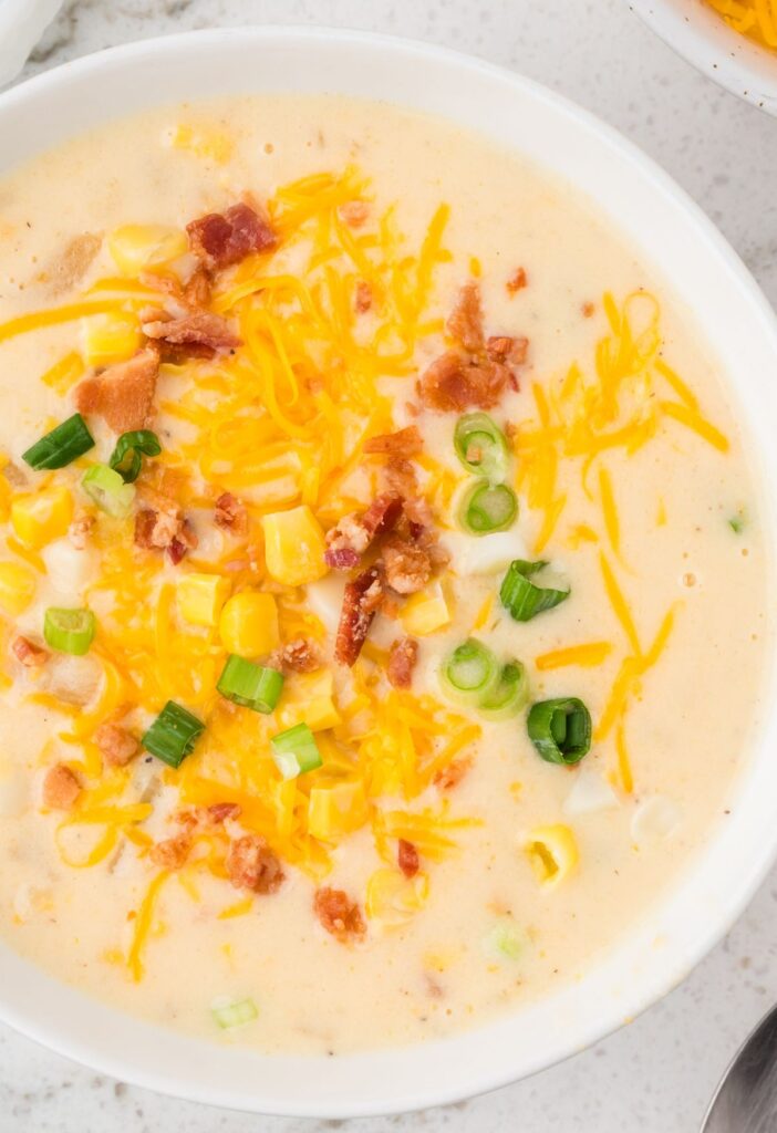 Top view of a white bowl with corn chowder and toppings.