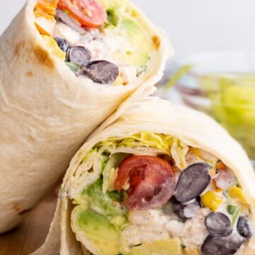 A chicken salad wrap cut in half and leaning on each other over a wooden cutting board.