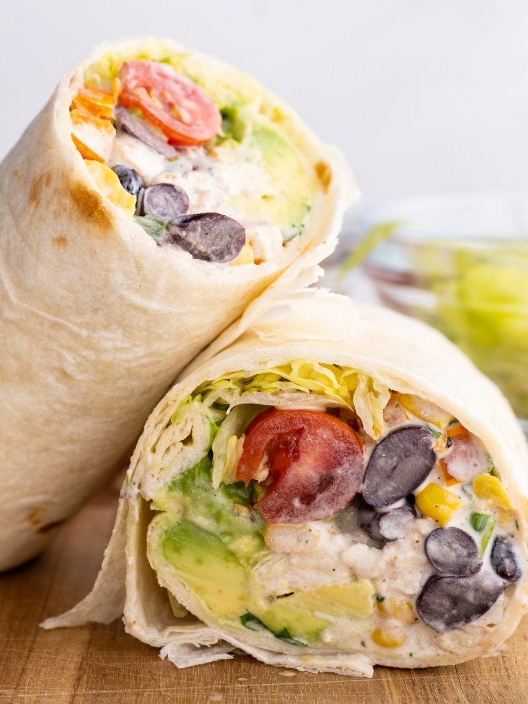 A chicken salad wrap cut in half and leaning on each other over a wooden cutting board. 