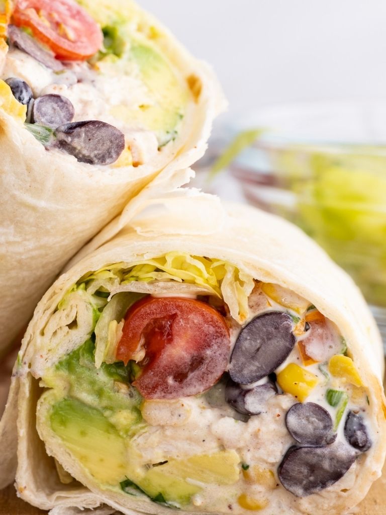 Close up shot of a halved chicken salad wrap cut in half and displayed on a wooden cutting board.