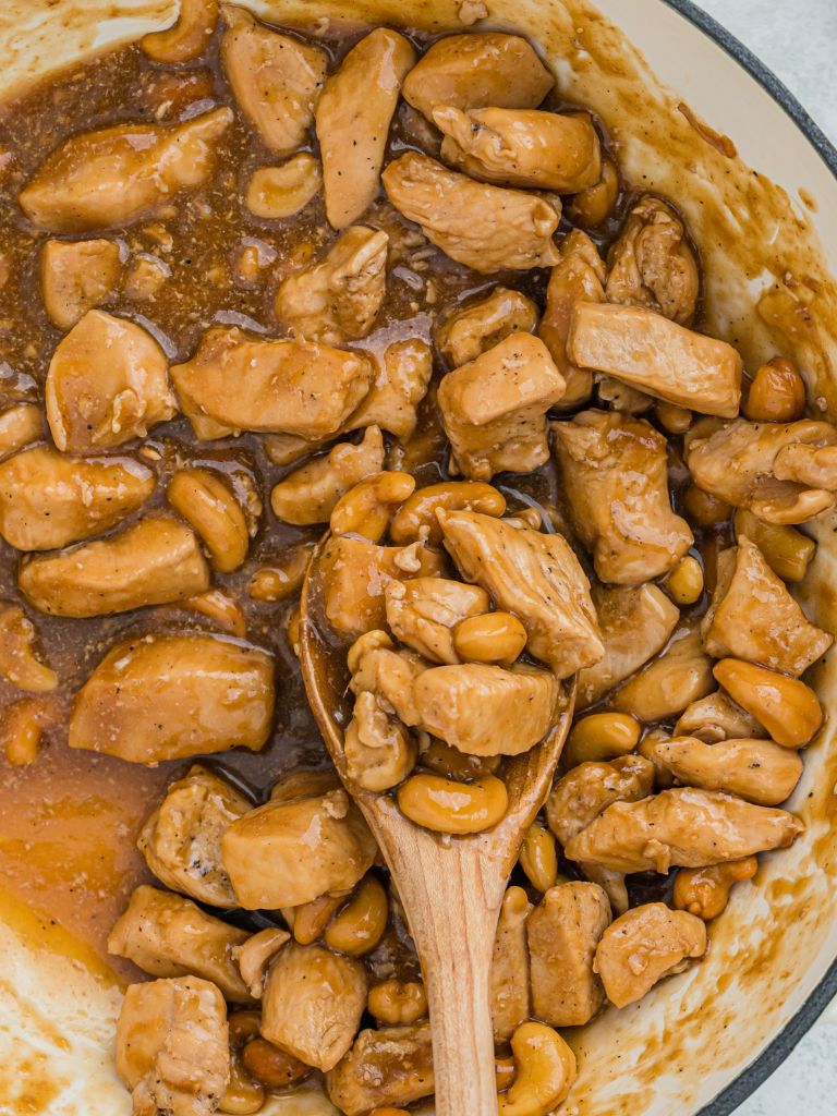 Skillet pan with chicken and sauce, with a wooden spoon in it. 