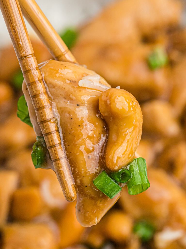 A chopstick with one bite of chicken on it and a cashew and green onion.