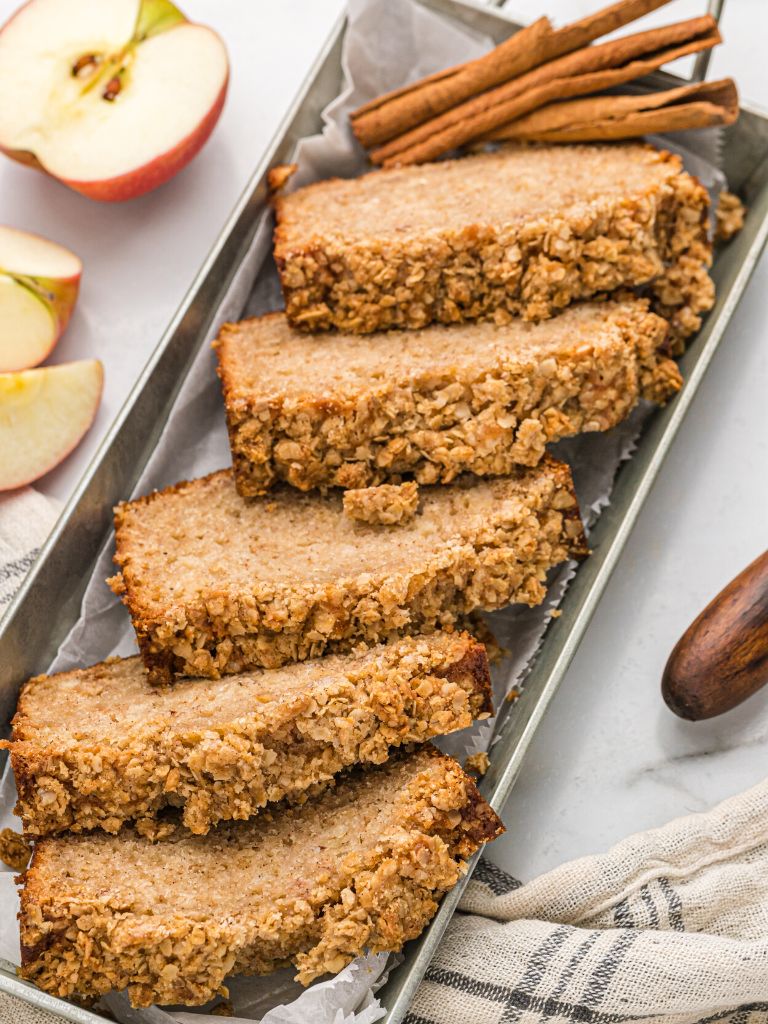 Tray of sliced quick bread with cinnamon sticks and apple chunks next to it. 