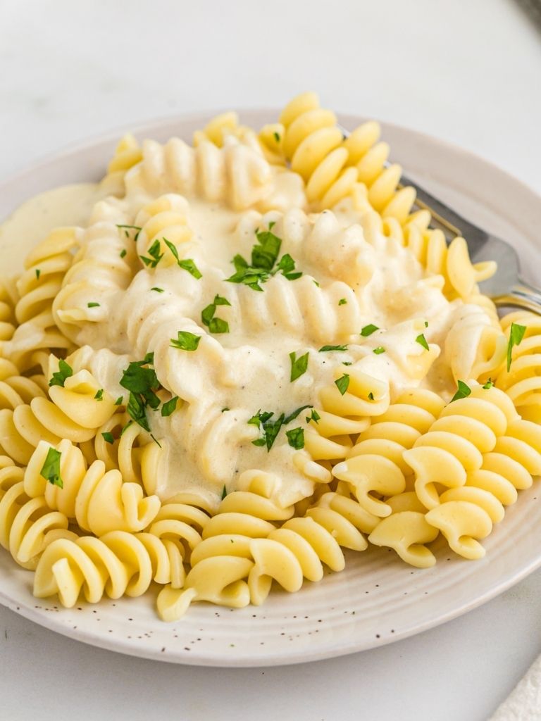 A plate with alfredo pasta on it and a fork.