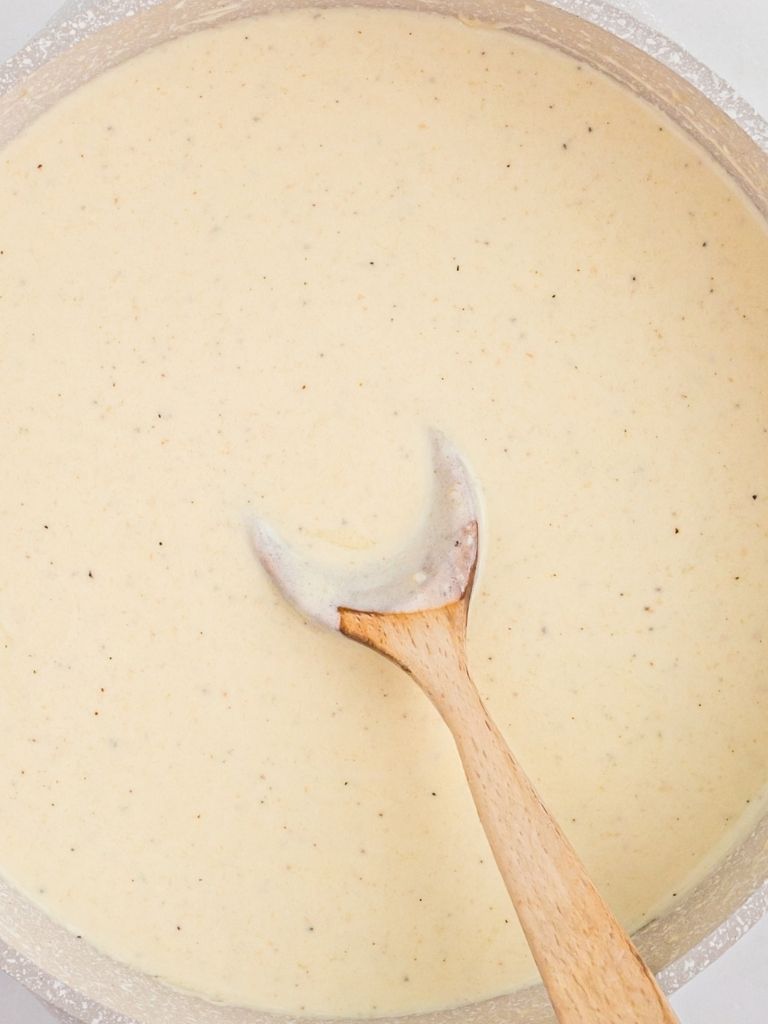 A pot of white alfredo sauce with a wooden spoon inside of it.