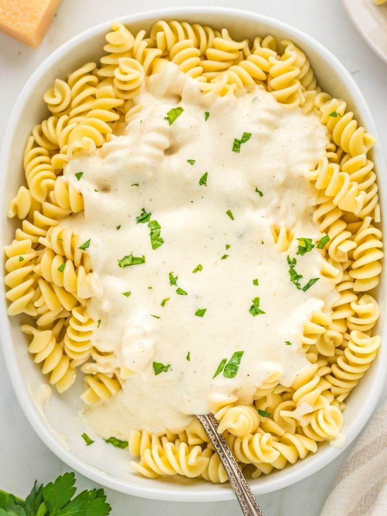 Rotini pasta in a white dish topped with alfredo sauce.