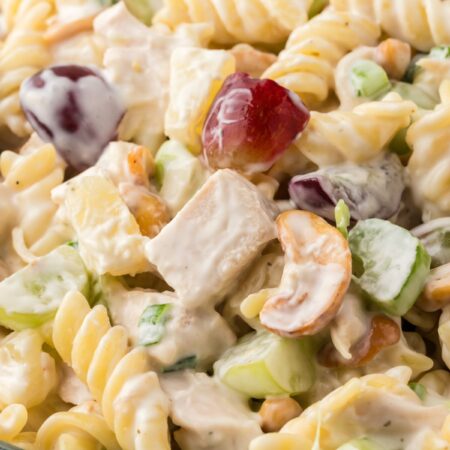A glass bowl of pasta salad with chicken grapes and pineapple