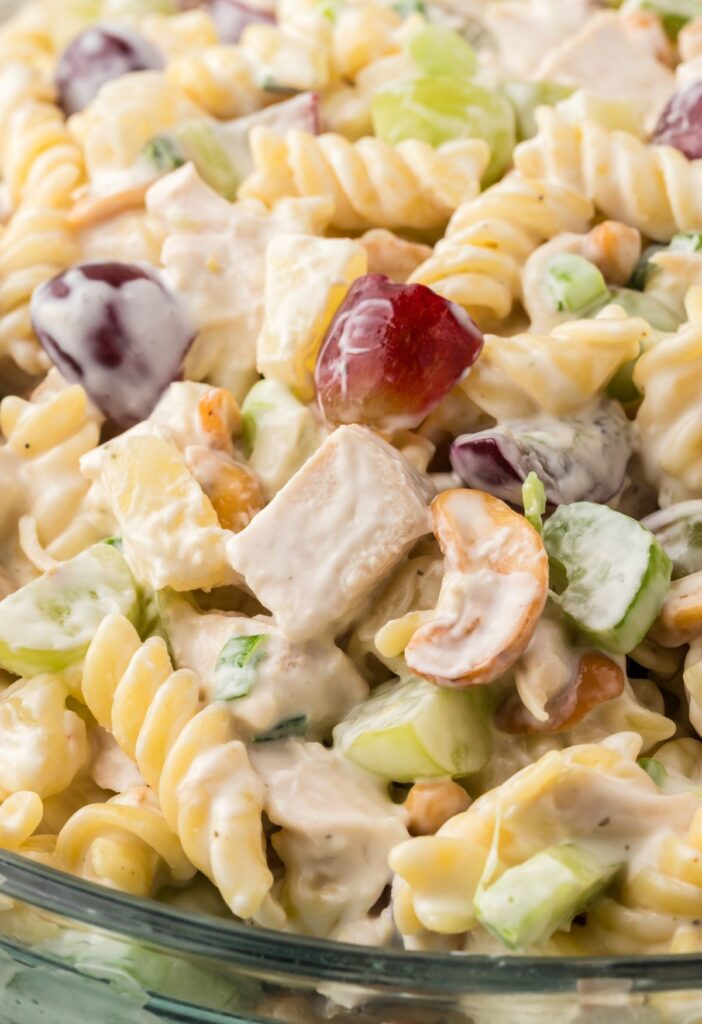 A glass bowl of pasta salad with chicken grapes and pineapple