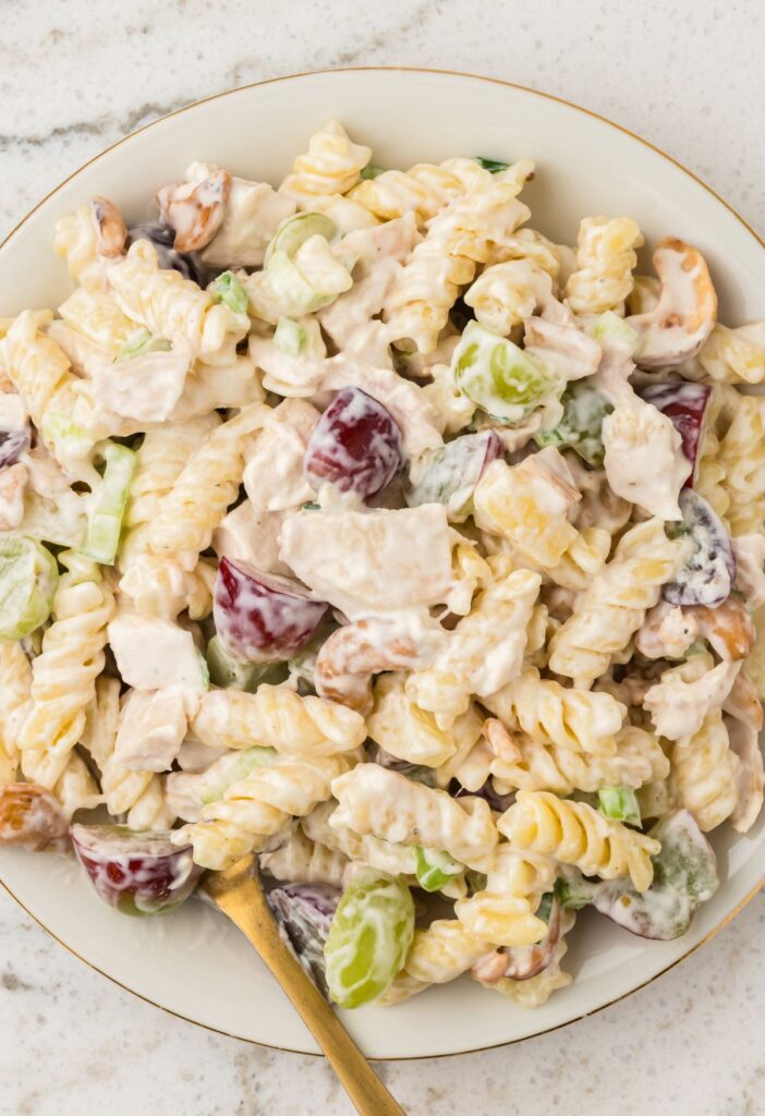 A white plate of chicken pasta salad with fruit