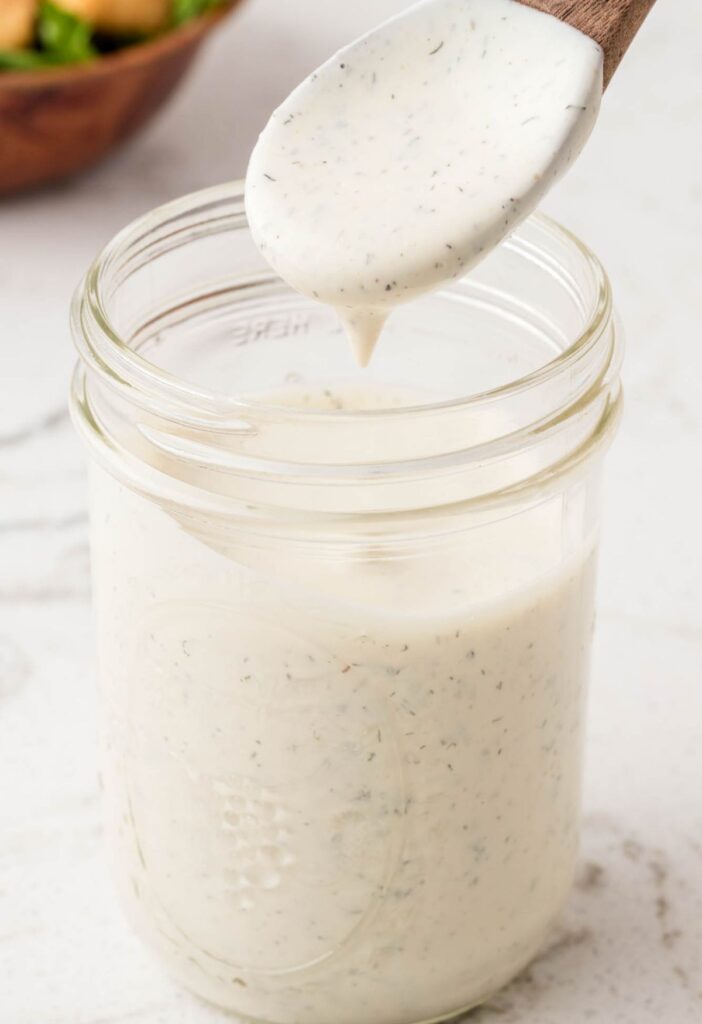 A jar of ranch dressing with a small wooden spoon 