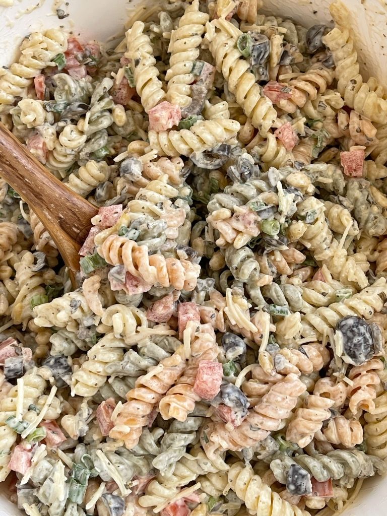 A bowl of pasta salad with a wooden spoon in it ready to serve. 