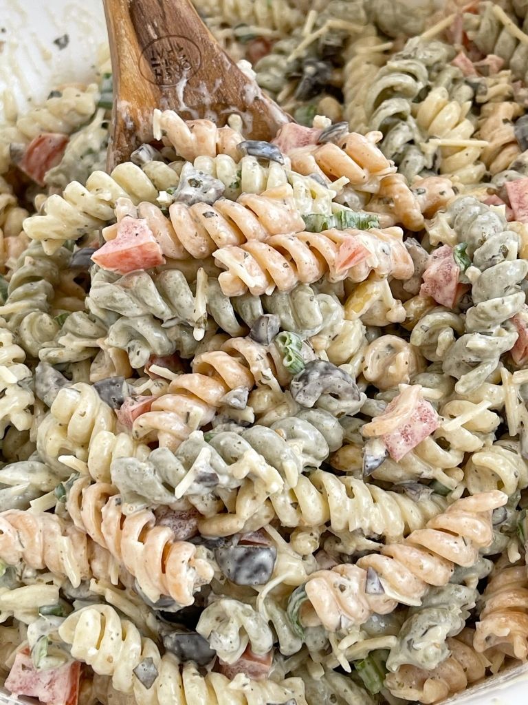 A scoop of pesto pasta salad on a wooden serving spoon. 