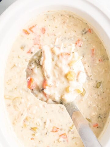 A slow cooker with creamy chicken wild rice soup with a scoop with some in it.
