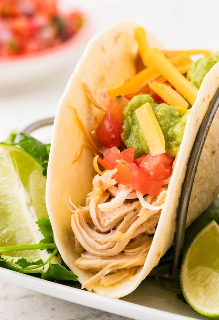 one taco with shredded chicken inside of it and toppings.