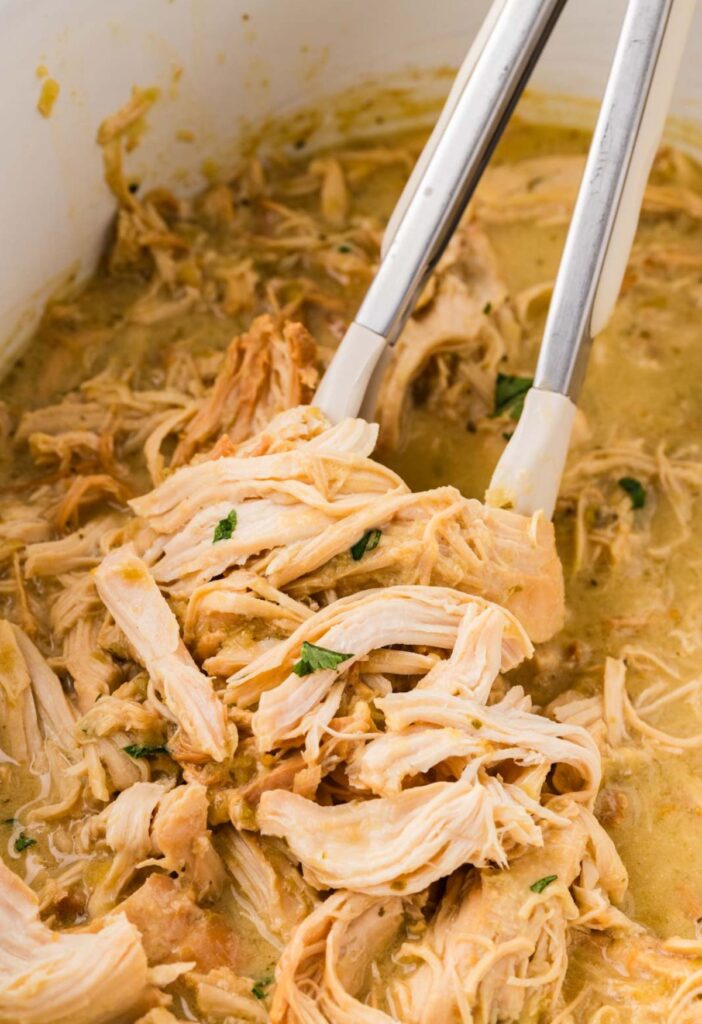 Inside of the crockpot with the shredded chicken being held with tongs.