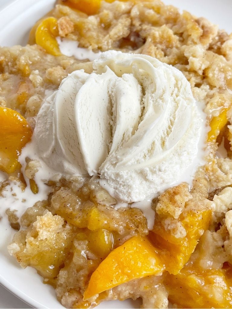 Peach dump cake on a white plate with ice cream melting on top.