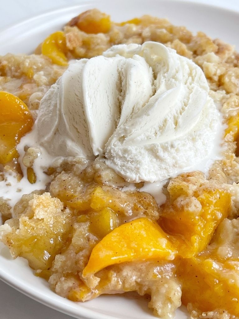 Plate of peach dump cake with ice cream on top.