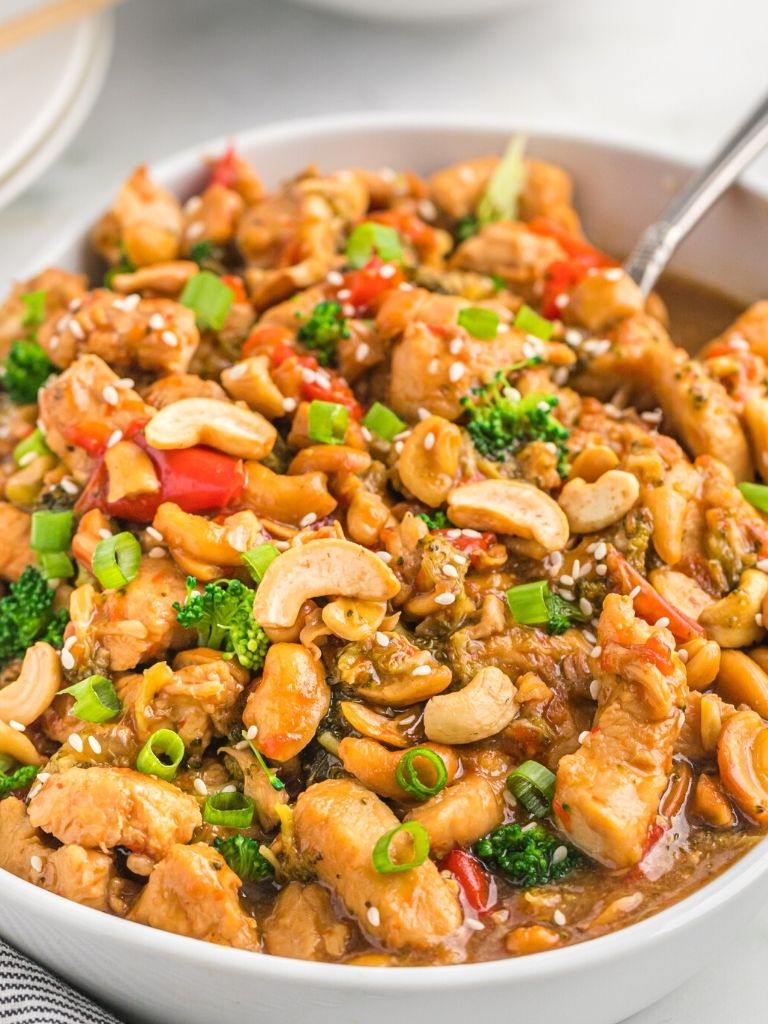 A white dish with cashew chicken inside of it and a spoon for serving. 