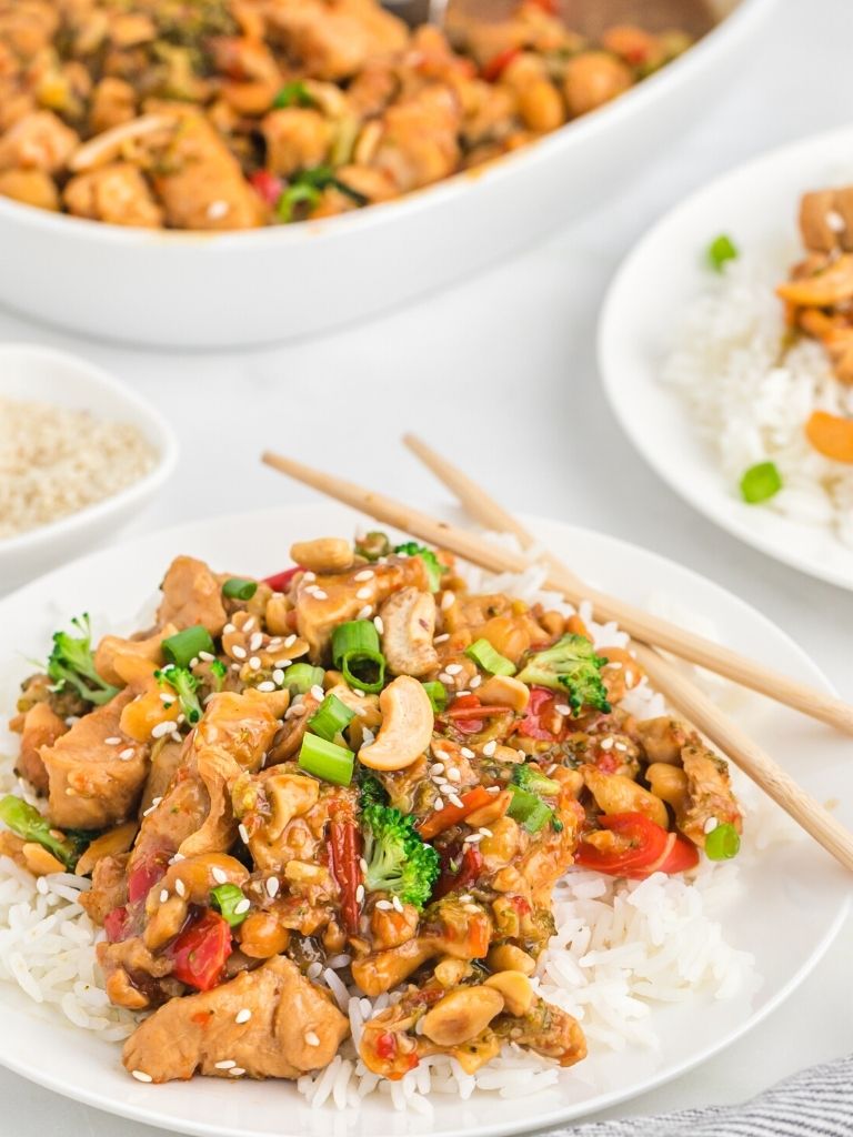 A plate of rice with cashew chicken on top with another plate of it in the background.