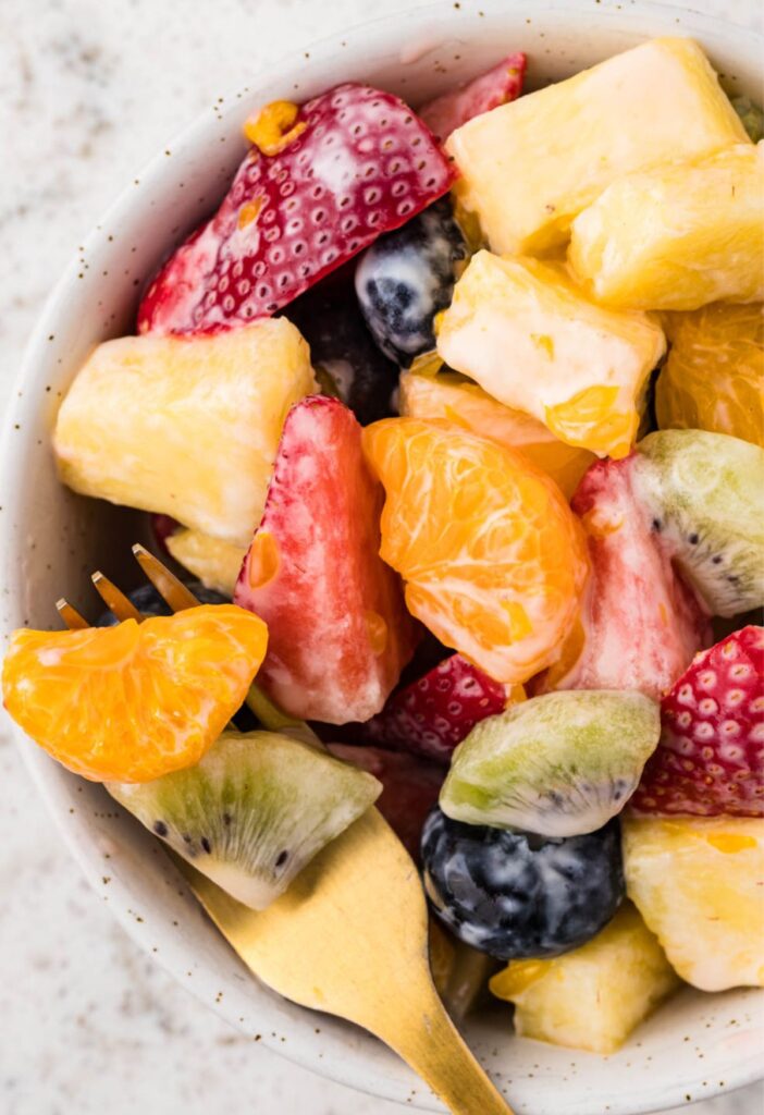 A small bowl with fruit salad in it and a fork