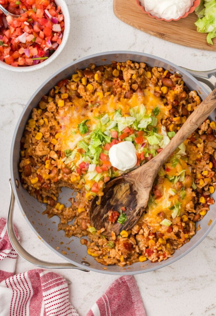 A one pot dinner recipe with taco toppings and wooden spoon. 