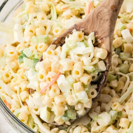 A bowl of pasta salad with coleslaw and a serving spoon with some salad on it.
