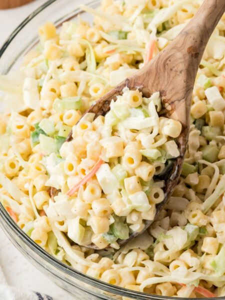 A bowl of pasta salad with coleslaw and a serving spoon with some salad on it.