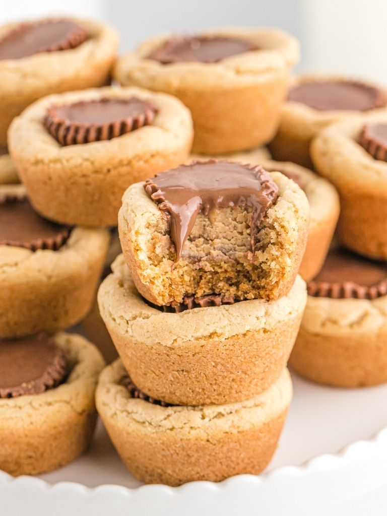 Stack of cookie cups on a white plate with the top having a bite taken out of it to show the inside.