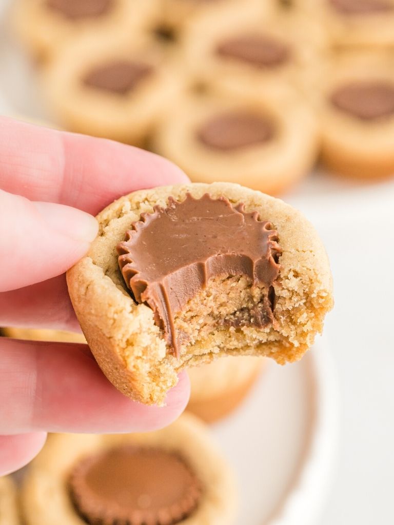 A hand holding a peanut butter cookie cup with a bite taken out of it.