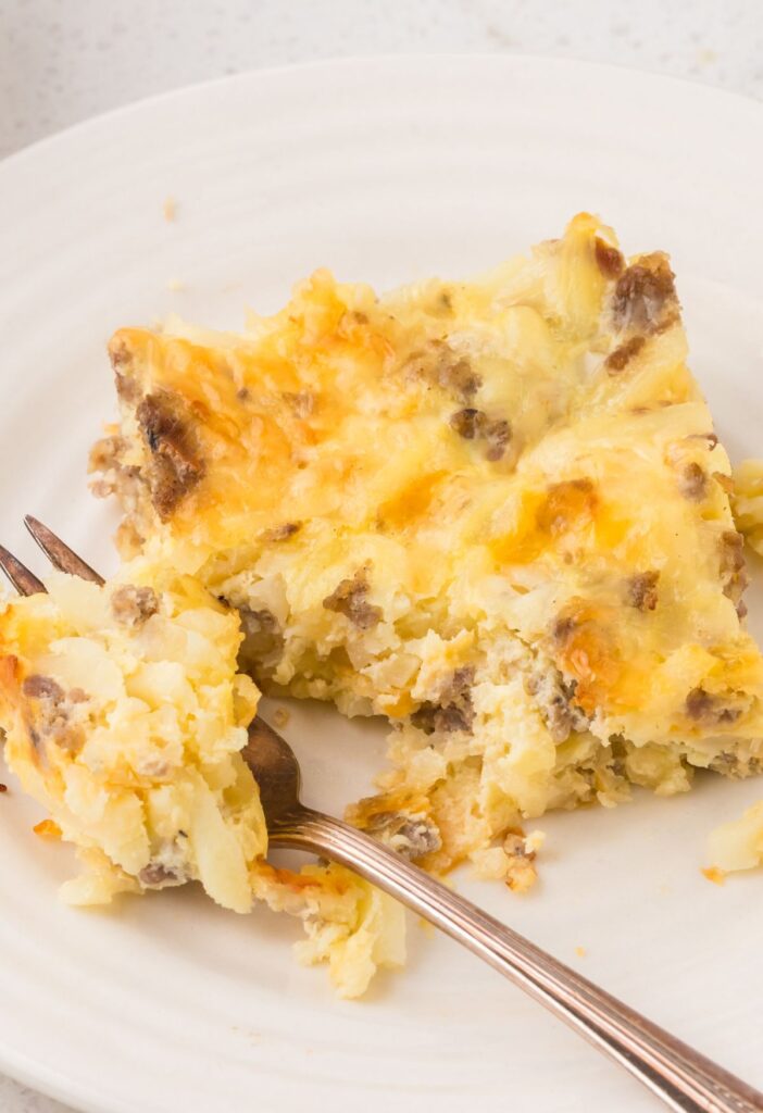 A piece of the breakfast casserole on a white plate with a fork next to it. 