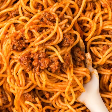 A skillet pan with spaghetti inside of it and a pasta serving spoon.
