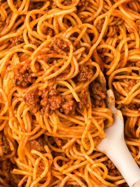 A skillet pan with spaghetti inside of it and a pasta serving spoon.