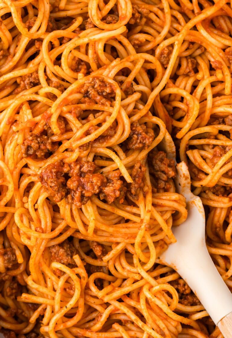 A skillet pan with spaghetti inside of it and a pasta serving spoon.