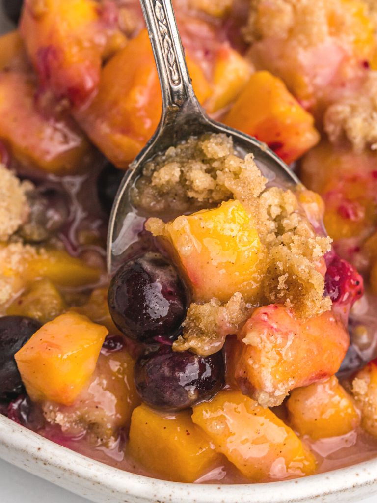 Close up shot of peaches and blueberries for this crisp recipe. A spoon with some on it.