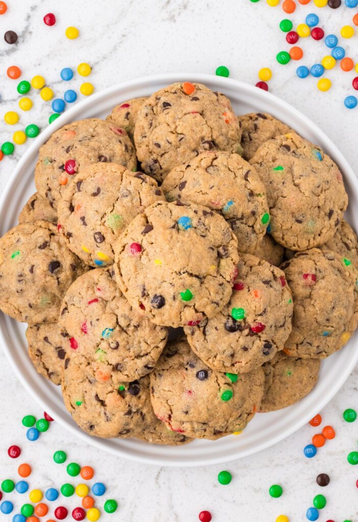 A plate of a stack of monster cookies with m&m's surrounding the plate.