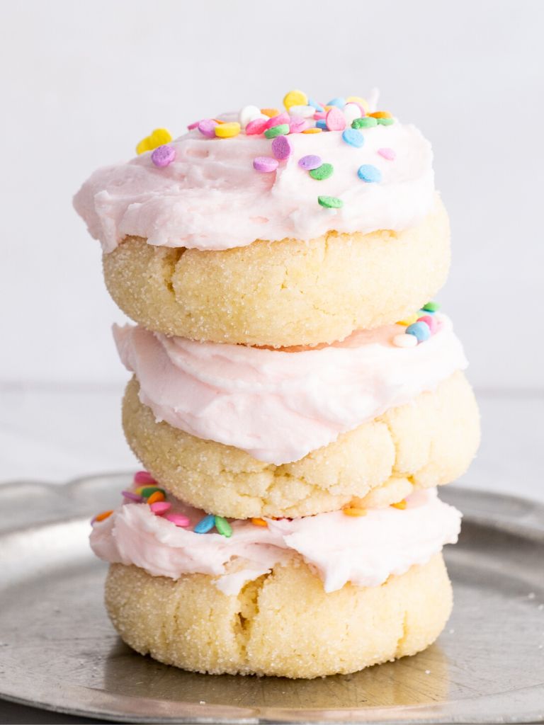 A stack of sugar cookies with pink frosting and sprinkles. 