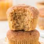 A stack of two muffins with the top having a bite taken out of it.