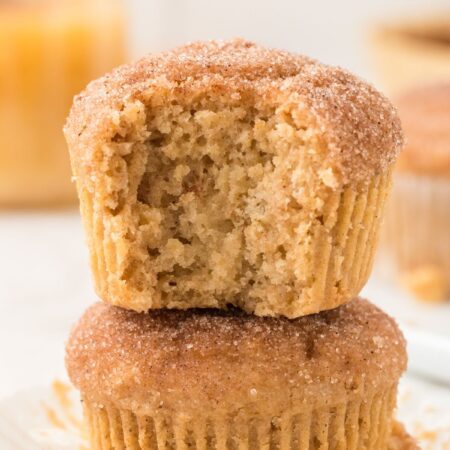 A stack of two muffins with the top having a bite taken out of it.