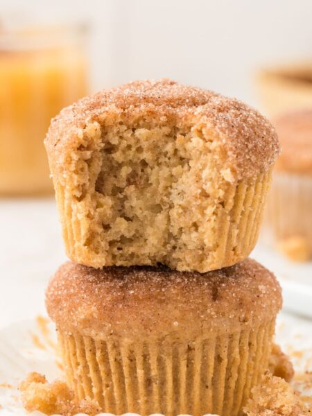 A stack of two muffins with the top having a bite taken out of it.