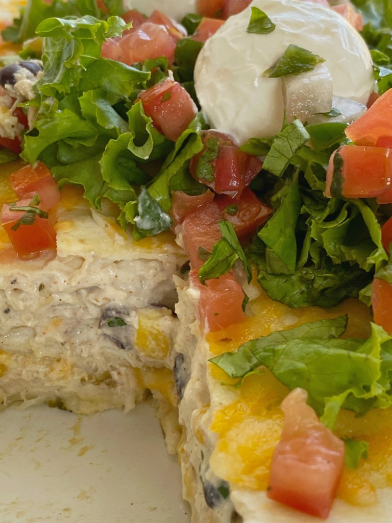Mexican Lasagna is layered with flour tortillas, cheese, and a creamy chicken mixture of black beans, corn, sour cream, salsa verde, and seasonings. An easy, one pan dinner that is best served with all the toppings. We love lettuce, pico de gallo, and sour cream!