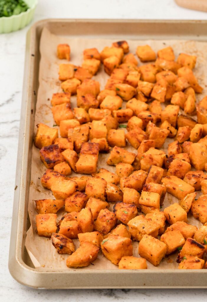 side view of the baking pan with sweet potatoes on it that have been roasted in the oven.
