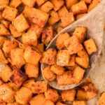 A pan of baked sweet potatoes with a wooden spoon holding some.