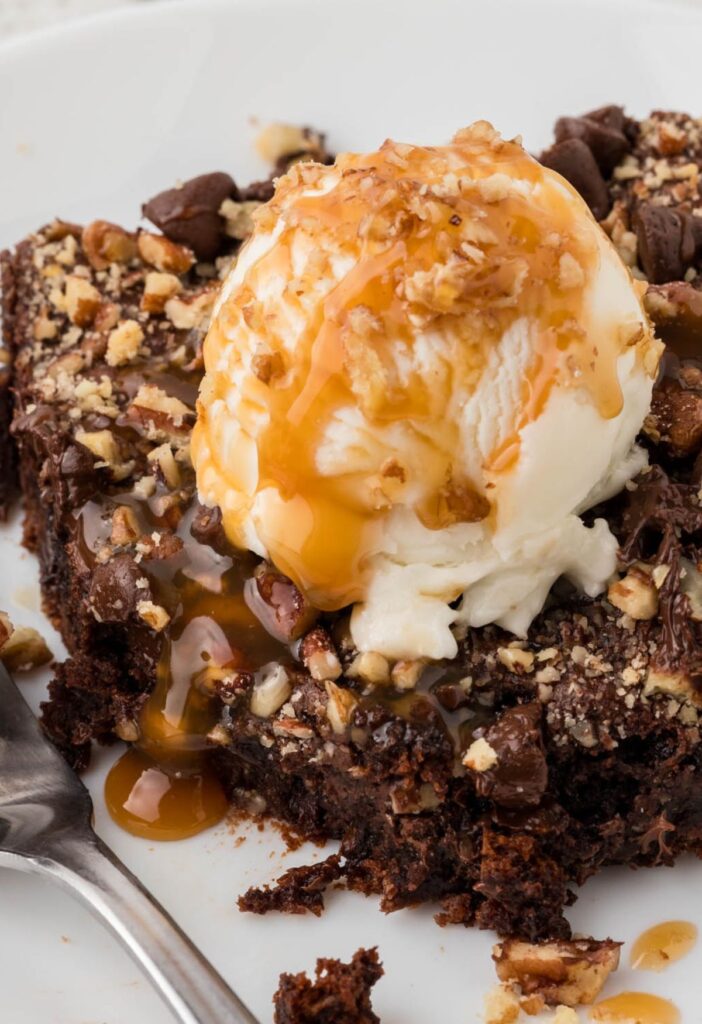 A serving plate of a slice of the dump cake with ice cream and caramel sauce on top. 